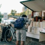 man in blue jacket and gray pants with blue backpack standing beside bicycle during daytime